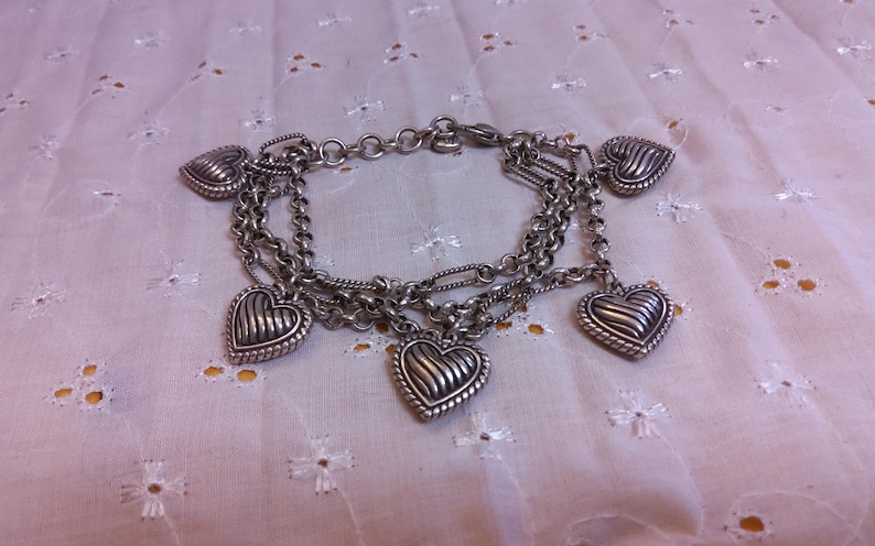 Pu&ograve; includere: Un braccialetto con ciondoli in argento con cinque ciondoli a forma di cuore. I ciondoli sono dettagliati con un design testurizzato e nervato.