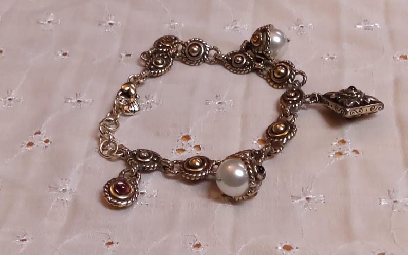 May include: Silver-toned bracelet with gold accents, featuring round and oval links. The bracelet includes pearl and gemstone charms. The design incorporates ornate detailing and a vintage aesthetic, suitable for jewelry enthusiasts.