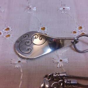 May include: A silver necklace with a pendant shaped like a spoon with a swirling design. The pendant is attached to a silver chain.