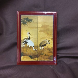 May include: A red leather-bound journal with a gold-leaf design featuring two cranes on a gold background. The cranes are depicted in a traditional Japanese style.