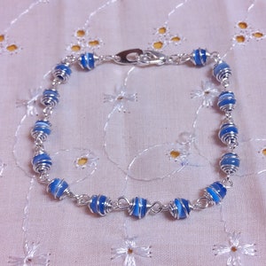 May include: A silver bracelet with blue and white striped beads wrapped in silver wire.