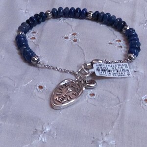 Puede incluir: Una pulsera de cuentas azules con un dije y cierre plateados. La pulsera presenta peque&ntilde;as cuentas azules redondas y cuentas plateadas. Un dije plateado con un dise&ntilde;o grabado cuelga de la pulsera. Una etiqueta est&aacute; adherida a la pulsera.