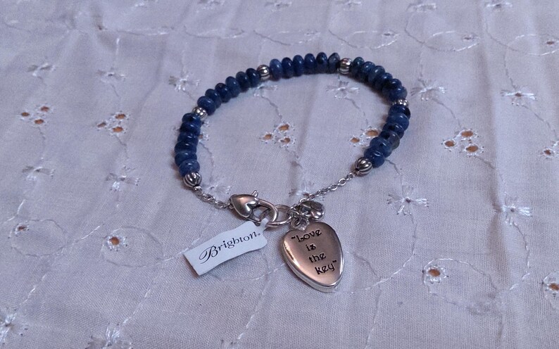 Puede incluir: Una pulsera de cuentas azules con detalles plateados y un dije en forma de coraz&oacute;n con la inscripci&oacute;n "Love is the key". La pulsera tiene un cierre plateado y una etiqueta "Brighton".