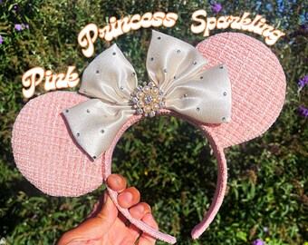 Peut inclure: Oreilles de Minnie Mouse roses scintillantes avec un nœud en satin blanc et des embellissements en perles. Les oreilles sont faites d'un tissu doux et texturé.