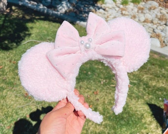 May include: Pink fuzzy mouse ears headband with a pink velvet bow with white pearl accents.