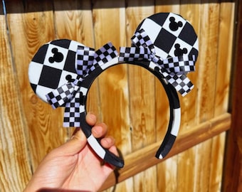 May include: Black and white checkered mouse ears headband with a black and white bow. The headband is made of fabric and has a black and white checkered pattern.
