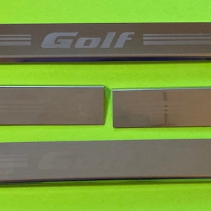 May include: Four silver metal car door sill trim pieces. The top piece has the word "Golf" engraved on it.