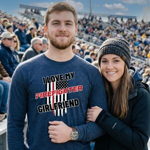 May include: A navy blue long-sleeve shirt with the text "I LOVE MY FIREFIGHTER GIRLFRIEND" in white and red, with an American flag design. A person is wearing a brown leather watch.