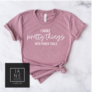 May include: A mauve t-shirt with the text "I make pretty things with power tools" printed in white.