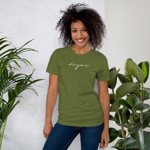 May include: A woman wearing a green short-sleeved t-shirt with the word "DIYer" written in white script on the front. She is wearing blue jeans and has curly brown hair.
