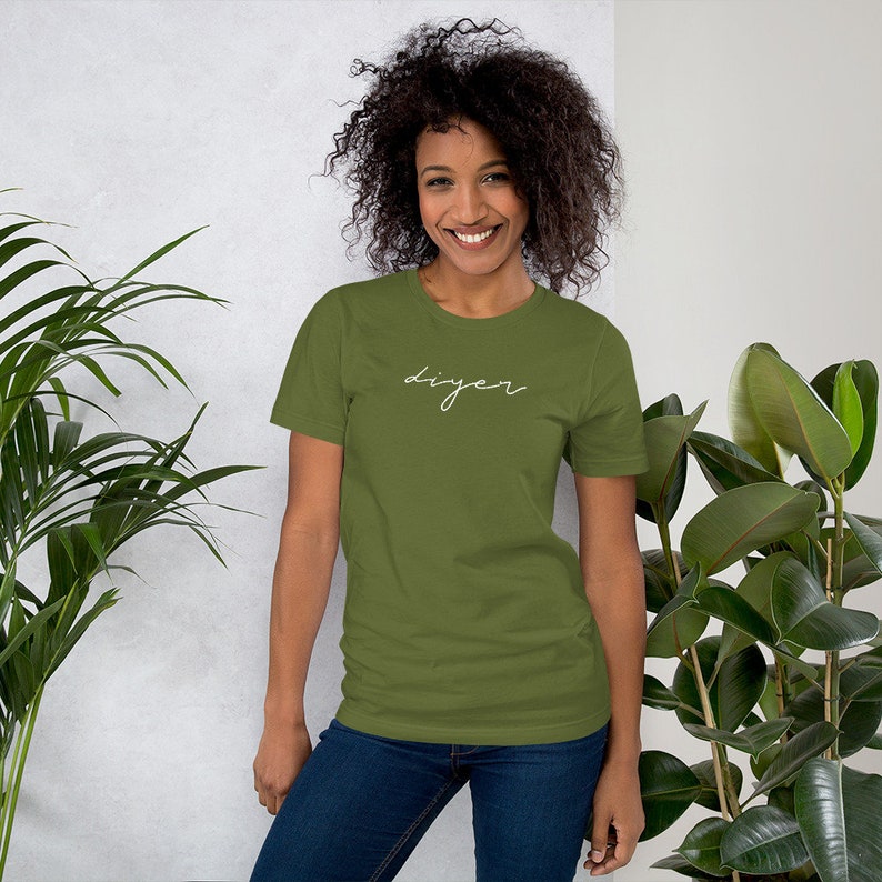 May include: A woman wearing a green short-sleeved t-shirt with the word "DIYer" written in white script on the front. She is wearing blue jeans and has curly brown hair.