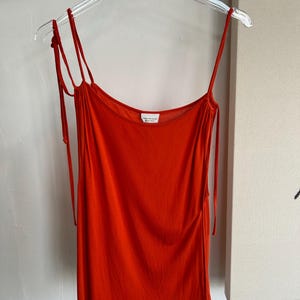 May include: A bright orange sleeveless top with thin straps that tie at the shoulders. The top has a scoop neck and a relaxed fit.