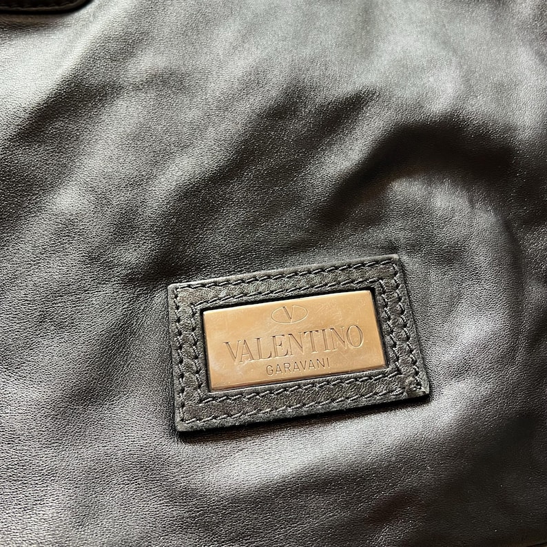 May include: Black leather handbag with a silver metal logo that reads "VALENTINO GARAVANI".