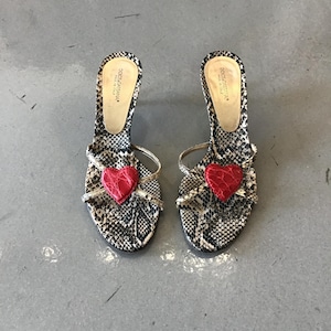 Puede incluir: Un par de sandalias de tacón Dolce & Gabbana. Las sandalias presentan un estampado de piel de serpiente con un corazón rojo en la parte delantera. Los tacones son negros y las correas finas y doradas. Hecho en Italia.