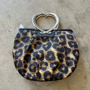 K&ouml;nnte beinhalten: Eine braune und schwarze Handtasche mit Leopardenmuster und einem silbernen herzf&ouml;rmigen Griff.