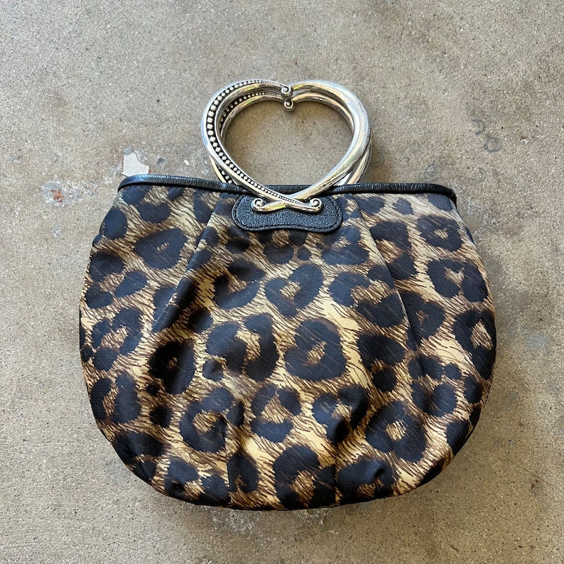 K&ouml;nnte beinhalten: Eine braune und schwarze Handtasche mit Leopardenmuster und einem silbernen herzf&ouml;rmigen Griff.