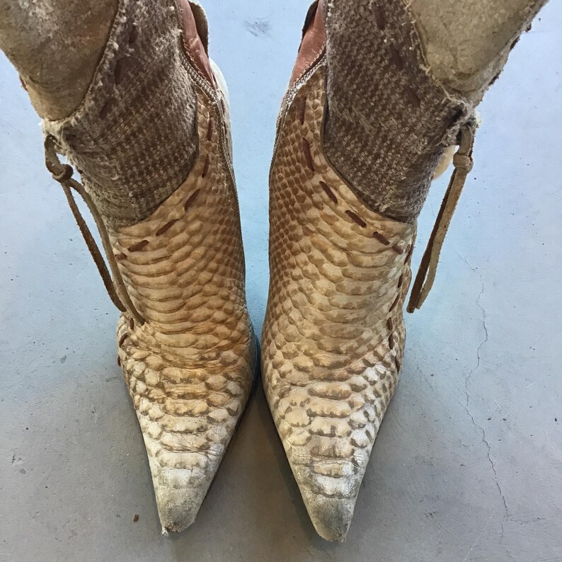 Op de afbeelding: Een paar beige en bruine laarzen met hakken en een slangenprint. De laarzen hebben spitse tenen en een rits aan de zijkant. Het bovenste deel van de laars is lichtbeige, terwijl het onderste deel een donkerder slangenpatroon heeft.