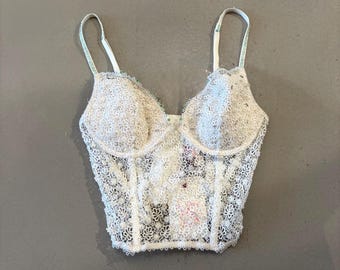 May include: White lace bustier with adjustable straps. The bustier features a floral pattern and a structured bodice. The straps are white with a hint of green. The garment is designed with a classic silhouette.