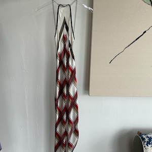 May include: A white halter dress with a geometric pattern in red, black, and brown. The dress has a fitted bodice and a flowing skirt.