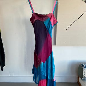Pode incluir: Um vestido sem mangas com um padrão degradê rosa, azul e roxo. O vestido tem uma bainha com babados e um corpete justo.