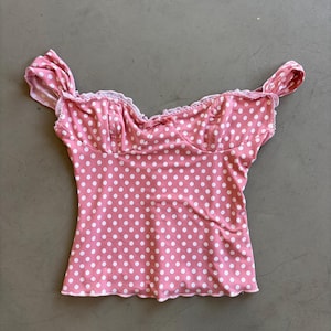 May include: Pink polka dot top with white dots. The top features a sweetheart neckline, ruffled sleeves, and a scalloped hem. The fabric is a soft, lightweight material.