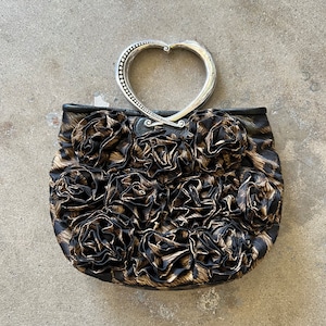 K&ouml;nnte beinhalten: Eine schwarze und braune Handtasche mit einem herzf&ouml;rmigen silbernen Griff und einem Blumendesign.