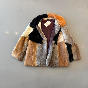 May include: A patchwork fur coat in a variety of colors including black, brown, orange, and cream. The coat has a quilted burgundy lining and a tag attached. The coat is a statement piece.