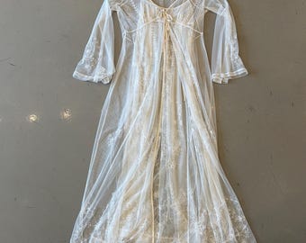 May include: A sheer, white, floor-length robe with long sleeves and delicate floral embroidery. The robe features a tie closure at the waist and a tag attached to the neckline. The garment is made of a lightweight, airy fabric.