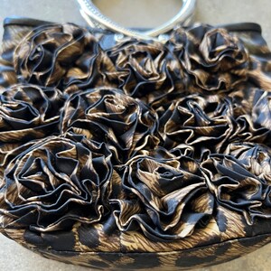 K&ouml;nnte beinhalten: Eine braune und schwarze Handtasche mit einem silbernen Henkel. Die Tasche ist aus Stoff und hat ein Blumenmuster.