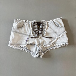 Op de afbeelding: Lichtblauwe denim shorts met een veter aan de voorkant en gerafelde randen. De shorts hebben twee voorzakken en een klein label aan de linkerkant. De shorts zijn lichtblauw.