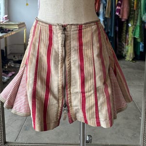 May include: A striped skirt with a zip fastening. The skirt is made from a lightweight fabric and has a ruffled hem. The skirt is red and white.