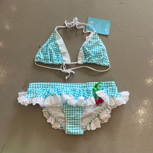 May include: A blue and white gingham bikini set. The triangle top and the bottoms have white lace trim. The bottoms feature a frilled edge and a small cherry decoration. The bikini is new with tags.