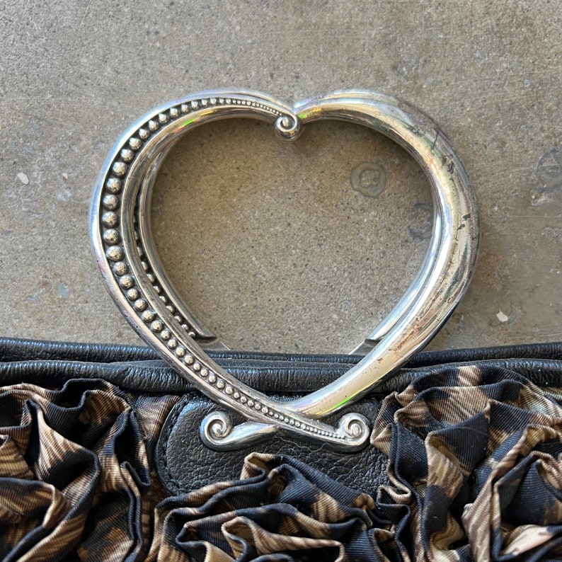 K&ouml;nnte beinhalten: Eine schwarze und braune Stoffhandtasche mit einem silbernen herzf&ouml;rmigen Griff. Der Griff ist mit kleinen Perlen verziert.