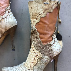 Op de afbeelding: Een paar laarzen met hoge hakken en een uniek ontwerp. De laarzen hebben een mix van materialen, waaronder slangenleer, leer en stof met patronen. Het kleurenpalet omvat bruin, beige en cr&egrave;me. De laarzen hebben spitse tenen en decoratieve stiksels.