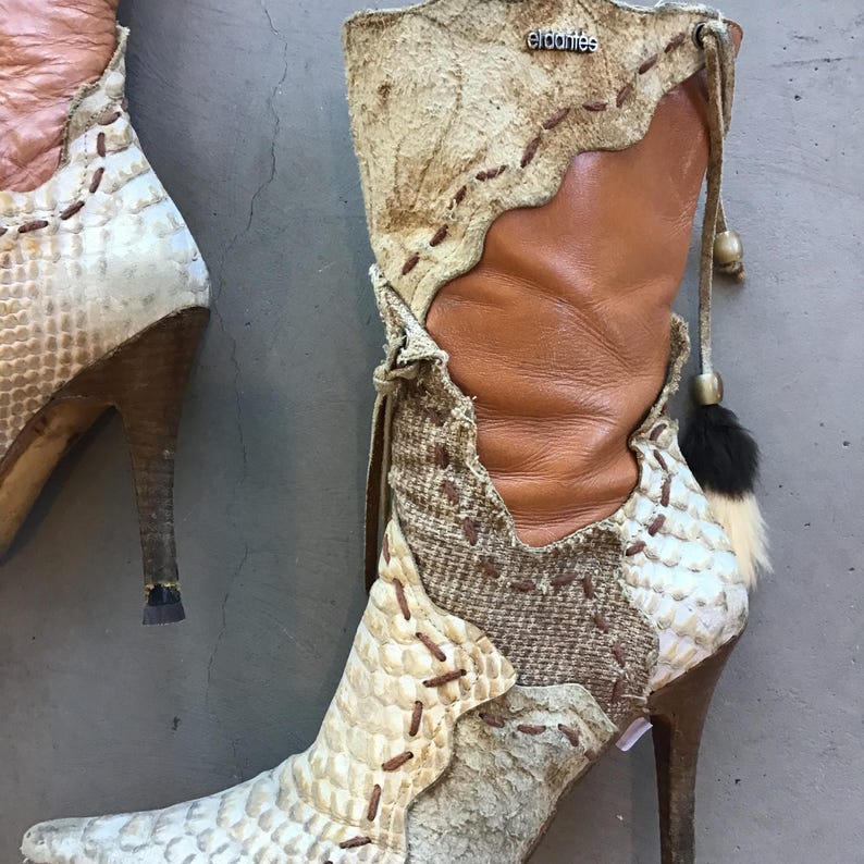 Op de afbeelding: Een paar laarzen met hoge hakken en een uniek ontwerp. De laarzen hebben een mix van materialen, waaronder slangenleer, leer en stof met patronen. Het kleurenpalet omvat bruin, beige en cr&egrave;me. De laarzen hebben spitse tenen en decoratieve stiksels.
