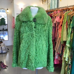 Peut inclure: Veste vert vif avec un design texturé et bouclé. La veste présente un col en fourrure vert assorti et une fermeture à boucle sombre. Elle est présentée sur un mannequin dans une boutique, avec des portants de vêtements colorés en arrière-plan.