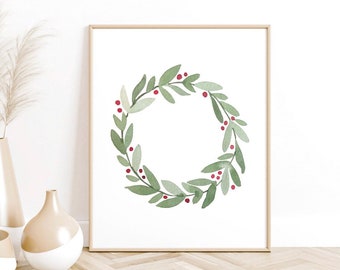 May include: A framed watercolor print featuring a green wreath with red berries. The wreath is composed of green leaves and small red berries, set against a white background. Decorative vases with beige and white accents are in the foreground.