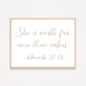 May include: A framed print with a white background and brown text that reads "She is worth far more than rubies."  The text is in a cursive font. Below the text is "~Proverbs 31:10".