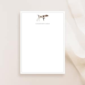 May include: White notepad with a black border. The top of the notepad features a watercolor illustration of a brown and white dog. The text "COURTNEY GRAY" is printed below the dog.