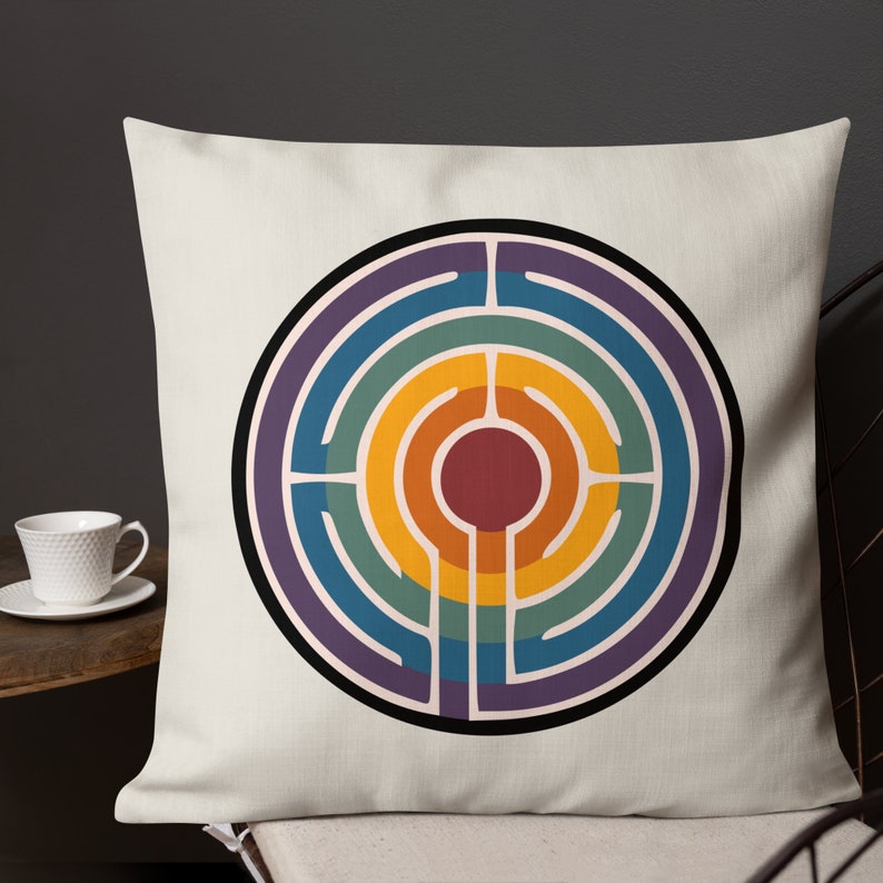 May include: A white throw pillow featuring a circular design. The design is a rainbow-coloured labyrinth with a red centre.