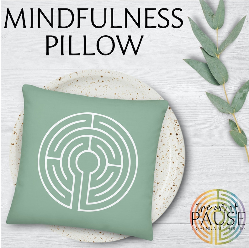 May include: A green square pillow with a white circular labyrinth design. The pillow is on a white plate with brown speckles. The text "the art of PAUSE creating a mindful life" is in the lower right corner of the image.