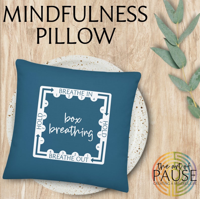 May include: A blue pillow with a white design that says "Breathe In", "Hold", "Breathe Out", and "box breathing". The design is a square with arrows pointing in a clockwise direction. The pillow is on a white plate.