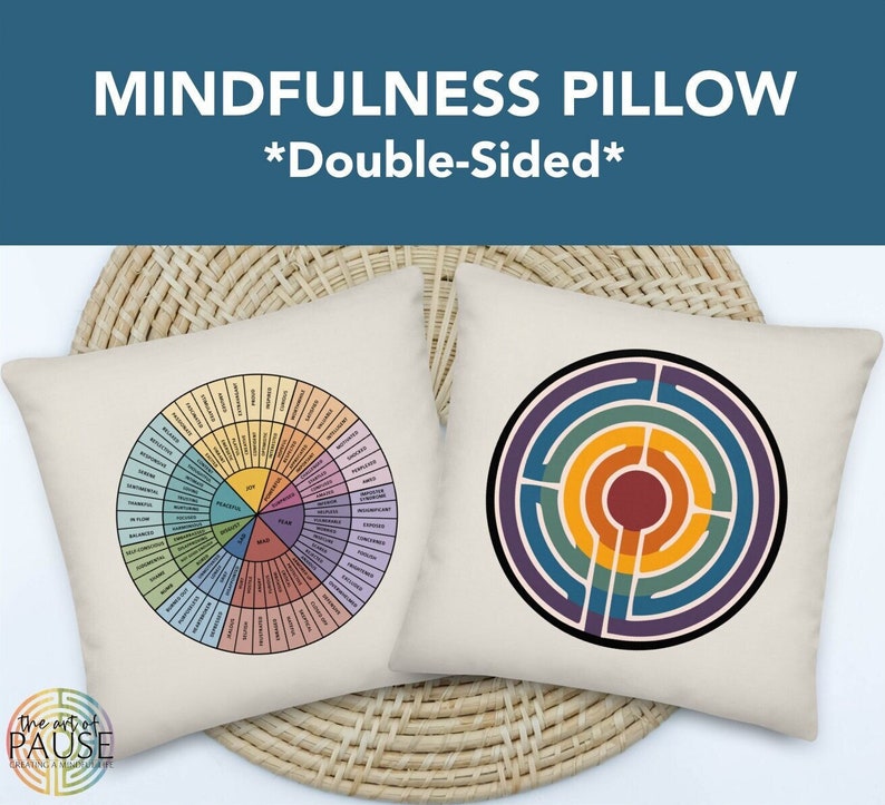 May include: A double-sided mindfulness pillow featuring a colourful wheel of emotions on one side and a labyrinth design on the other. The pillow is made of white fabric and has a beige background.