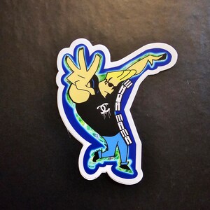 May include: A cartoon character with blonde hair and a black shirt with the text "EDDIE" and "MAMA" on it. The character is wearing blue jeans and is making a peace sign with their hand. The background is a green and blue swirl.
