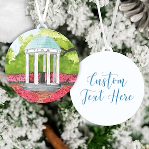 May include: A round white ornament with a watercolor illustration of the Old Well on the UNC Chapel Hill campus. The ornament has a white ribbon for hanging and a second blank ornament with the text "Custom Text Here" in blue.