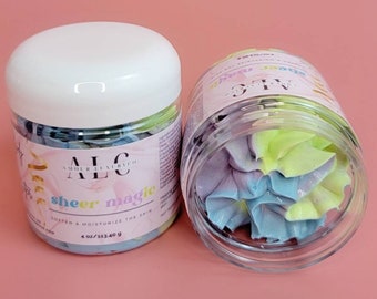 Può includere: Due vasetti trasparenti di burro per il corpo con coperchi bianchi. I vasetti sono etichettati "ALC Amour Luxury Co. sheer magic" e contengono sapone a forma di fiore dai colori pastello. Ogni vasetto è da 113 g.