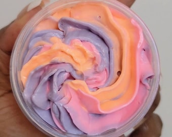 Può includere: Un contenitore di plastica trasparente pieno di panna montata colorata. La panna è mescolata con sfumature di rosa, arancione e viola. Il contenitore è tenuto in una mano.
