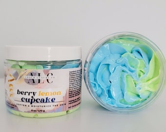 Può includere: Due vasetti trasparenti di burro per il corpo, uno aperto e uno chiuso. Il burro per il corpo è mescolato con colori blu e verdi. L'etichetta recita "berry lemon cupcake" e "soften & moisturize the skin". Ogni vasetto contiene 170 g.