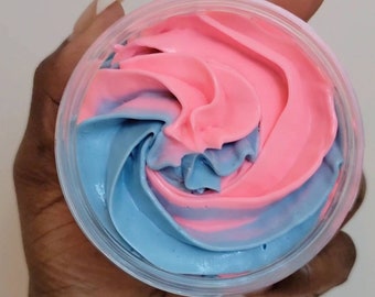 May include: A clear plastic container filled with pink and blue whipped cream. The cream is swirled together, creating a marbled effect. The container is held in a hand.