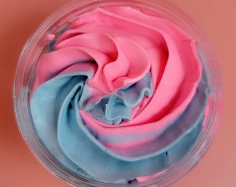 May include: A clear plastic container filled with pink and blue whipped cream. The cream is swirled together, creating a marbled effect. The background is a solid pink color.
